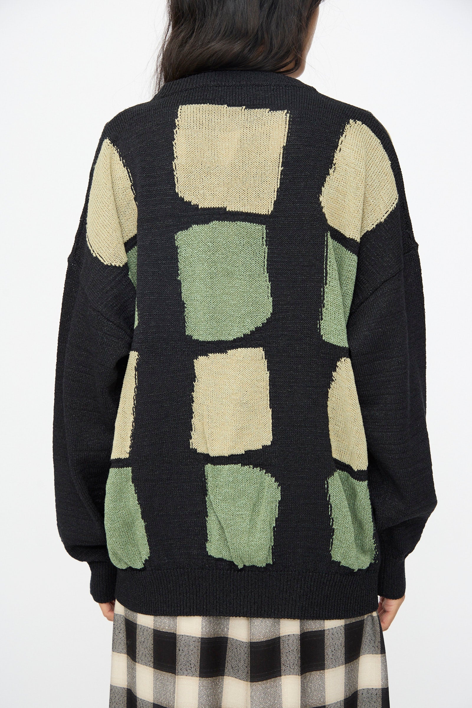 A person wears the Cristaseya Washi Paper Patchwork Sweater in Black with Sage and Light Khaki, paired with a black and white checkered skirt.
