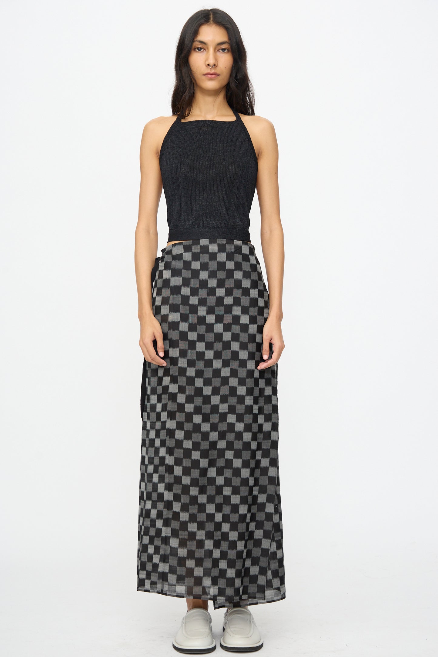 A woman stands against a white background wearing the Cristaseya Washi Paper Summer Top in Black, paired with a long black and gray checkered skirt and light-colored shoes.