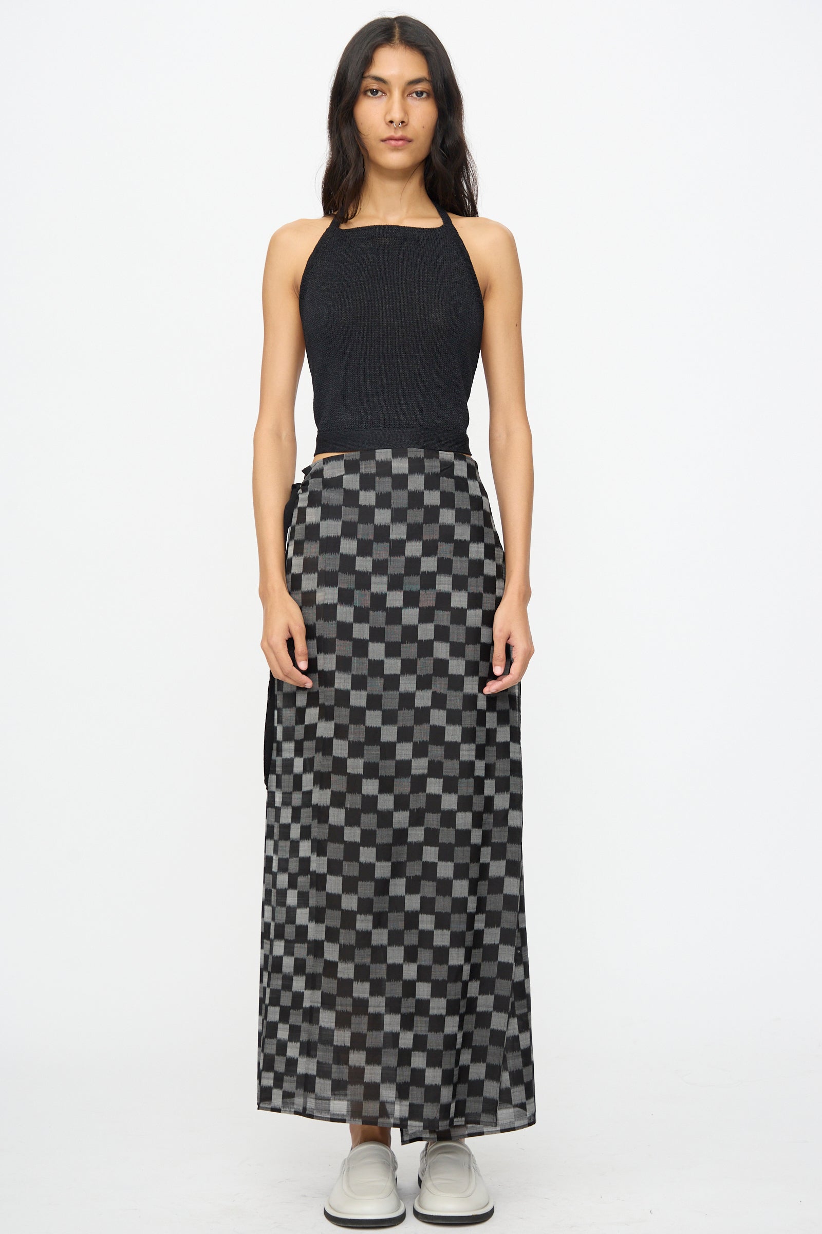 A woman stands against a white background wearing the Cristaseya Washi Paper Summer Top in Black, paired with a long black and gray checkered skirt and light-colored shoes.
