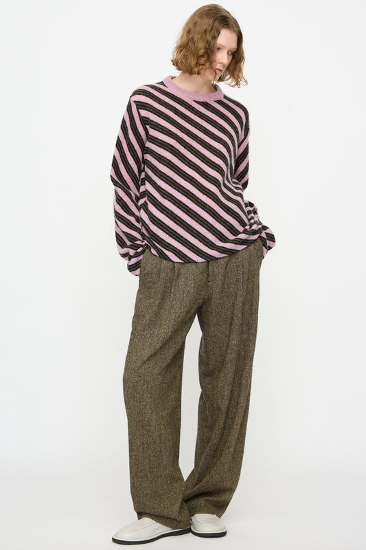 A person wearing the Cristaseya Wool Diagonal Striped Sweater in Taupe and Pink, paired with wide brown trousers and white shoes, standing against a plain white background.