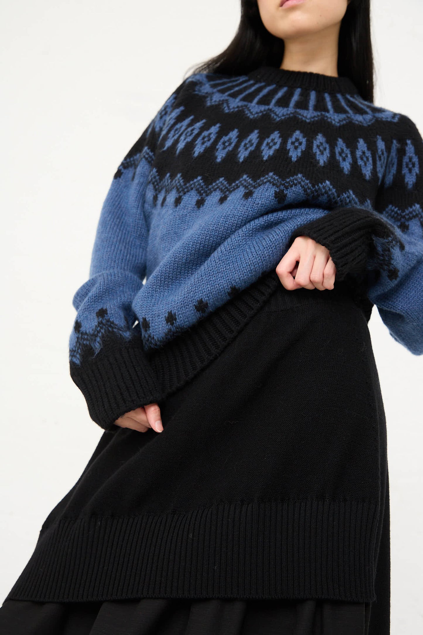 Person wearing a blue and black patterned sweater made in Italy and the Cristaseya Wool Patched Long Skirt in Black, standing against a neutral background.