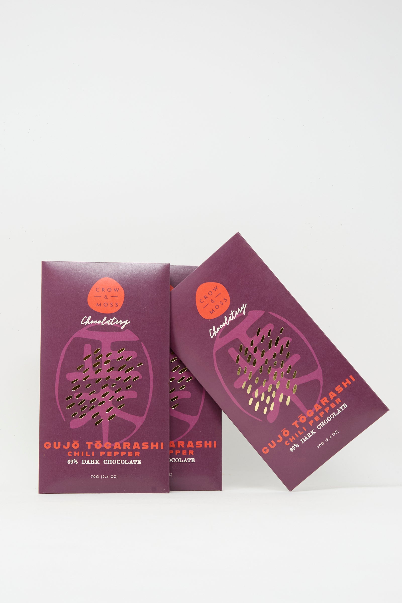 Three purple packages of Crow & Moss Togarashi Chili Dark Chocolate Bar, made with single-origin cacao, are arranged against a plain white background.