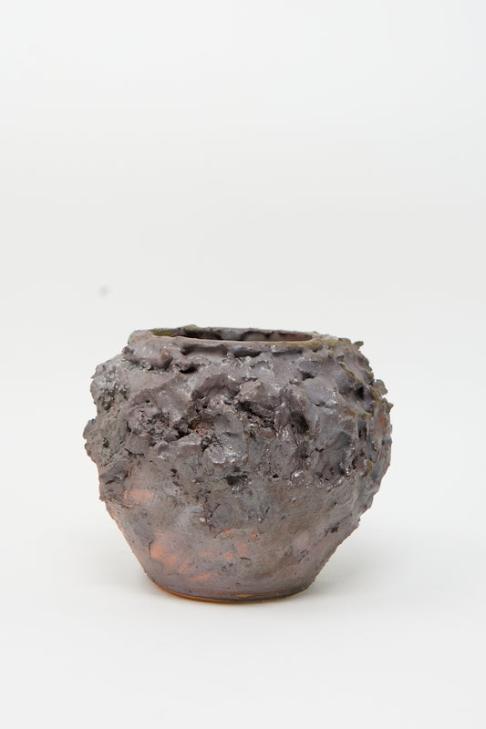 The Ash Bloom N. 17 Vase by Dear You is a textured, dark brown ceramic pot with a rough, uneven surface reminiscent of hand-built vases, set against a plain white background.