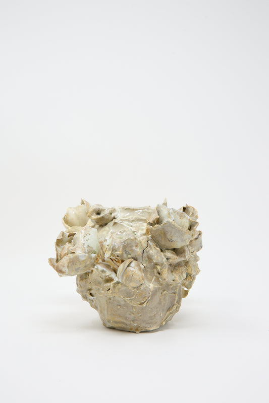 A one-of-a-kind ceramic sculpture with a rough, irregular surface and multiple protrusions in a light beige color, reminiscent of a hand-built vase, stands against a plain white background. This unique piece is the Ash Bloom N14 Vase by Dear You.
