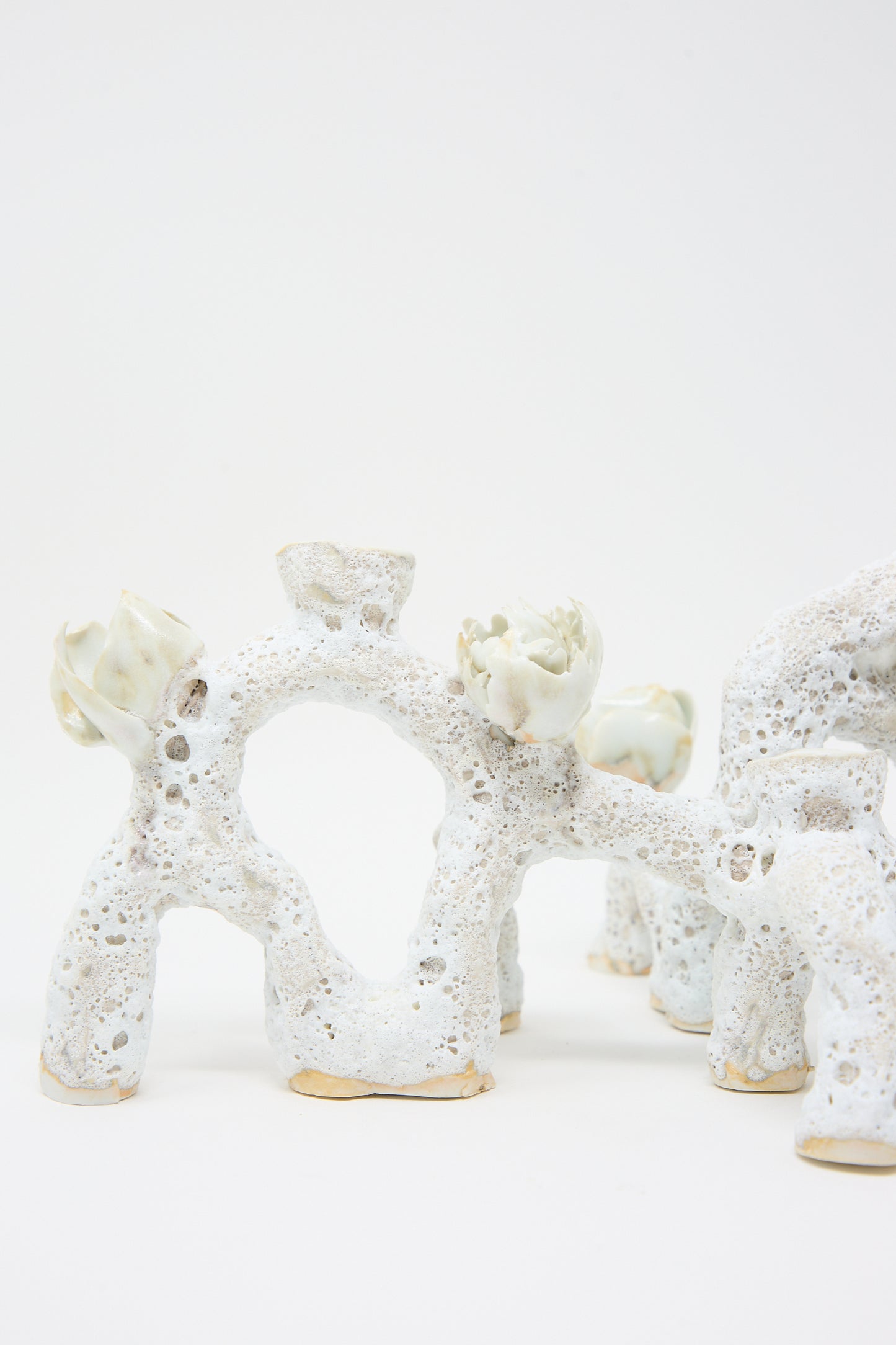 Abstract hand-built ceramic sculpture with a porous, white texture and numerous small arch-like formations. The piece features organic elements resembling flower buds or plant shapes, evoking luminescent petals. This is the Blooming Arches Candle Holder by Dear You.