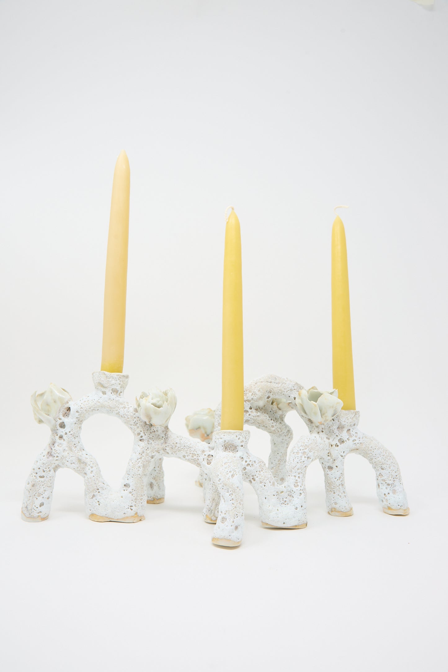 A hand-built, ceramic candle holder with a speckled, arch-like design elegantly cradles three tall, yellow candles on a plain white background is the Blooming Arches Candle Holder by Dear You.