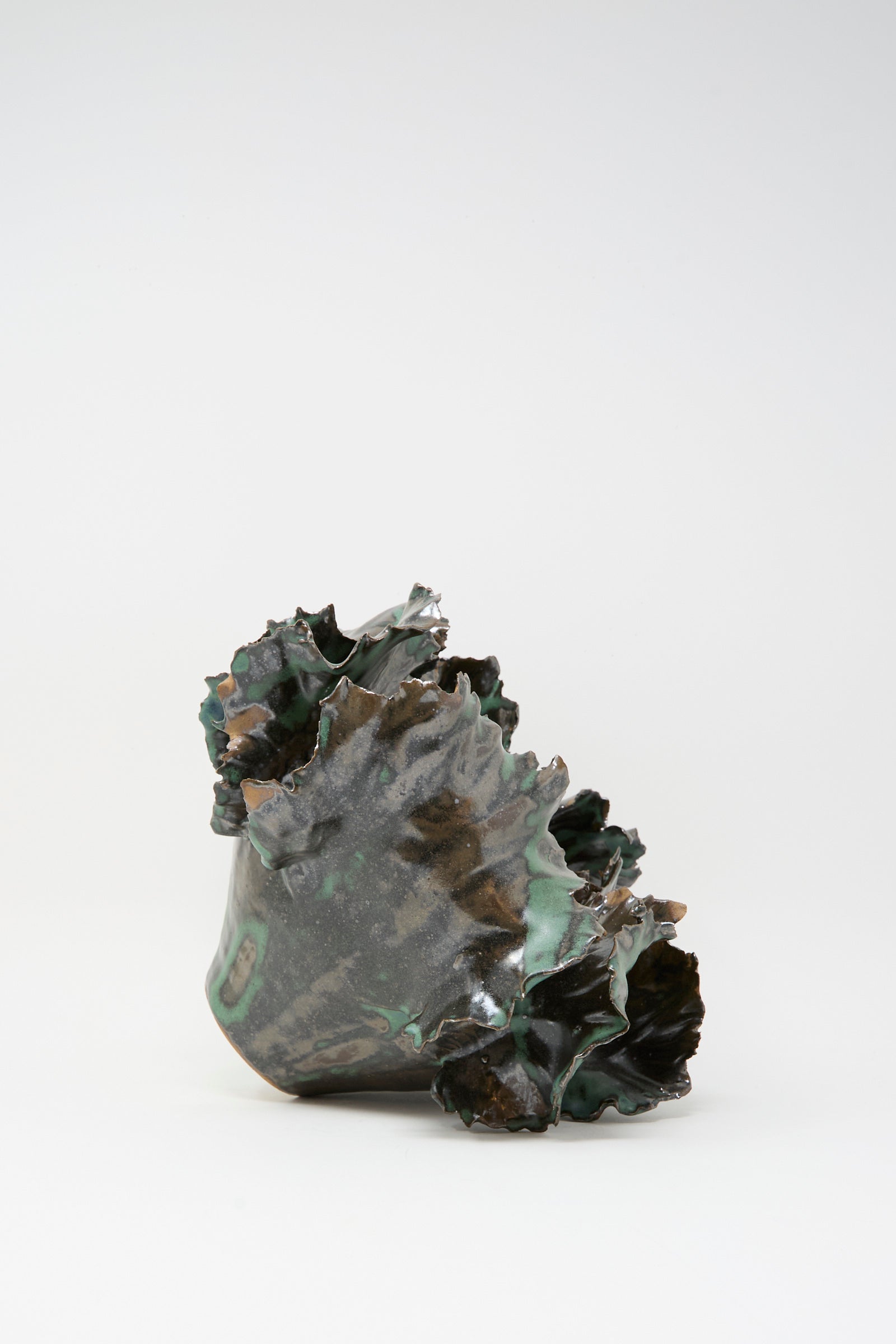 Wild Petals Iris N.5 in Green by Dear You: an abstract ceramic sculpture featuring wavy, textured edges and a dark green, glossy finish, reminiscent of a porcelain vase, set against a plain white background.