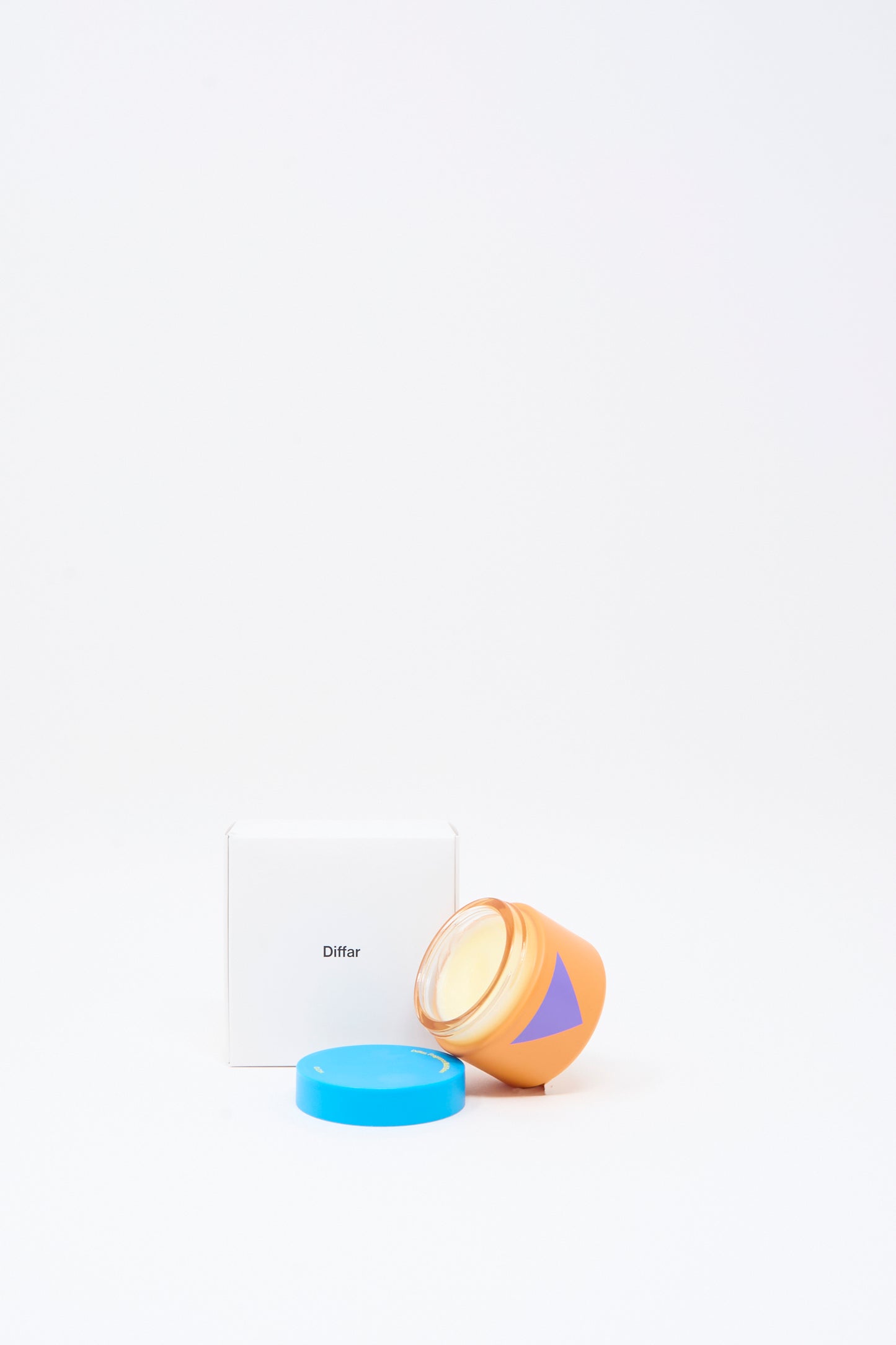 An orange jar with a blue lid and a purple triangle, containing Diffar's Fragrance Multi Balm in Fresh Moss, sits beside a white box labeled “Diffar” on a plain white background.