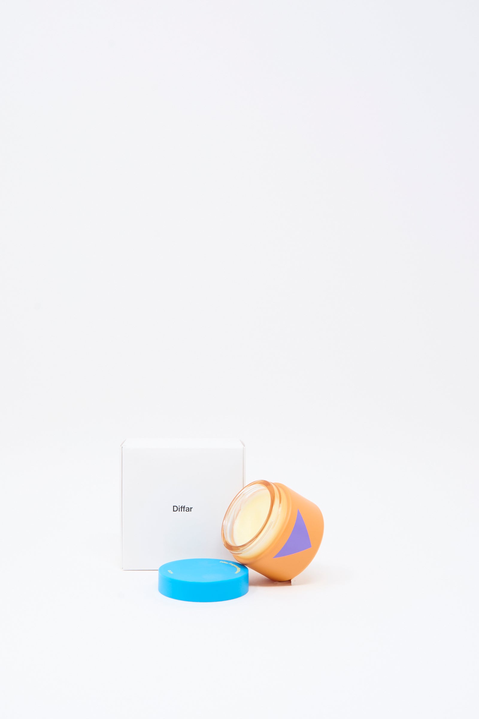 An orange jar with a blue lid and a purple triangle, containing Diffar's Fragrance Multi Balm in Fresh Moss, sits beside a white box labeled “Diffar” on a plain white background.