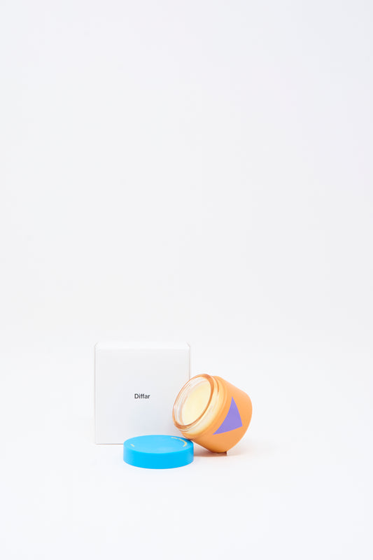 An orange jar with a blue lid and a purple triangle, containing Diffar's Fragrance Multi Balm in Fresh Moss, sits beside a white box labeled “Diffar” on a plain white background.