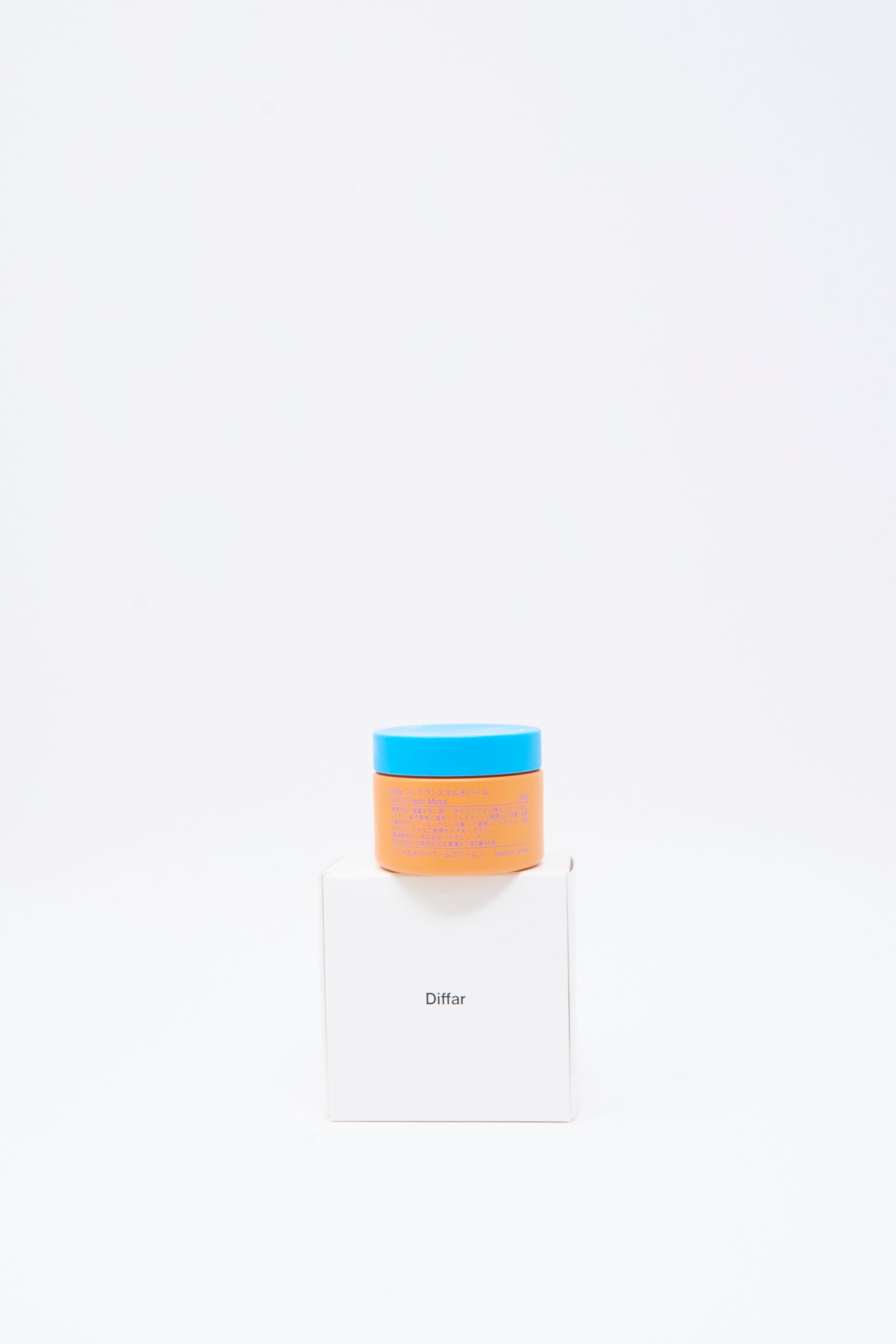 A small orange jar of Diffar’s Fragrance Multi Balm in Fresh Moss, topped with a blue lid, sits on a white box labeled "Diffar" against a plain white background.