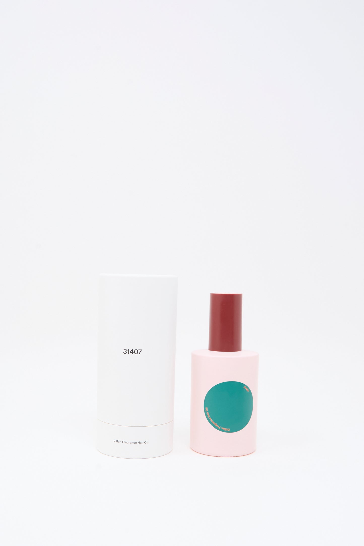 A pink bottle with a red cap and a green circle label, containing Diffar Herbal Floral Fragrance Oil infused with plant-based essential oils, stands next to a tall white cylindrical box labeled "31407" against a plain white background.