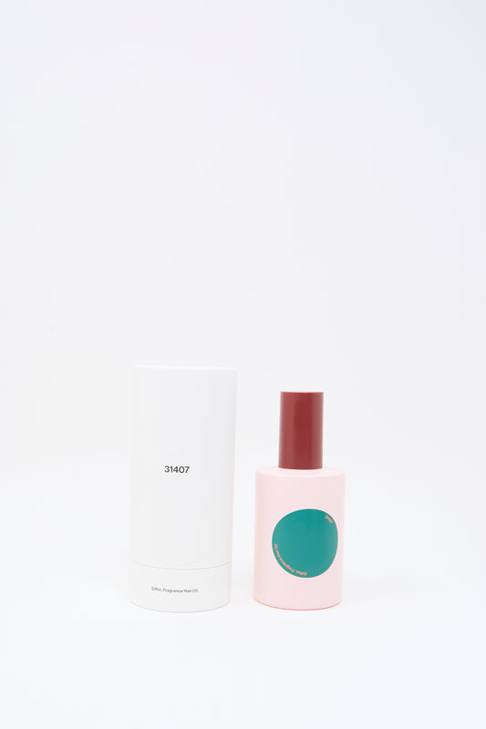 A pink bottle with a red cap and a green circle label, containing Diffar Herbal Floral Fragrance Oil infused with plant-based essential oils, stands next to a tall white cylindrical box labeled "31407" against a plain white background.