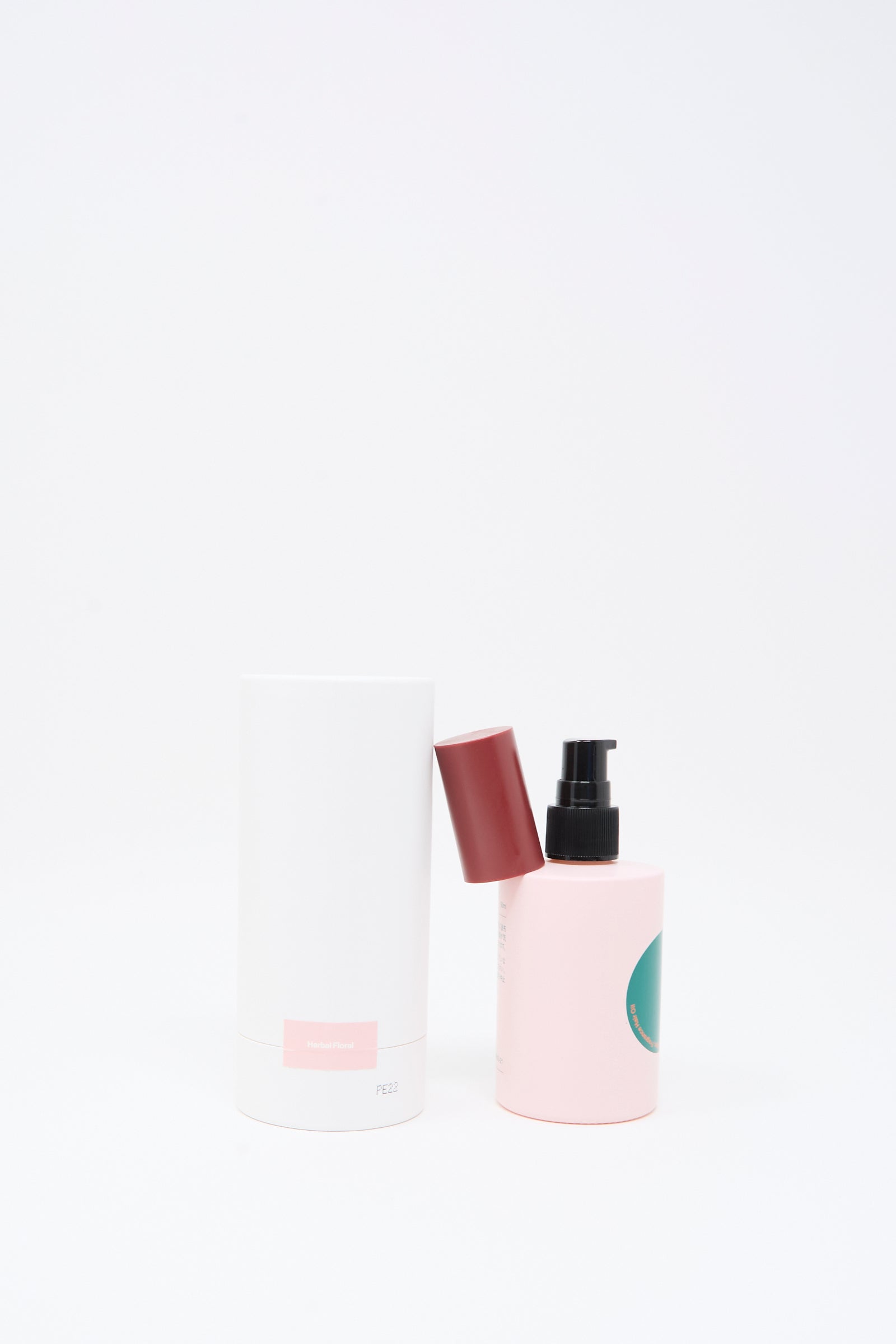 Two cosmetic containers from Diffar’s Herbal Floral Fragrance Oil collection are displayed: one tall white cylinder with a maroon cap, and one pink pump bottle with a black dispenser, set against a plain white background. 