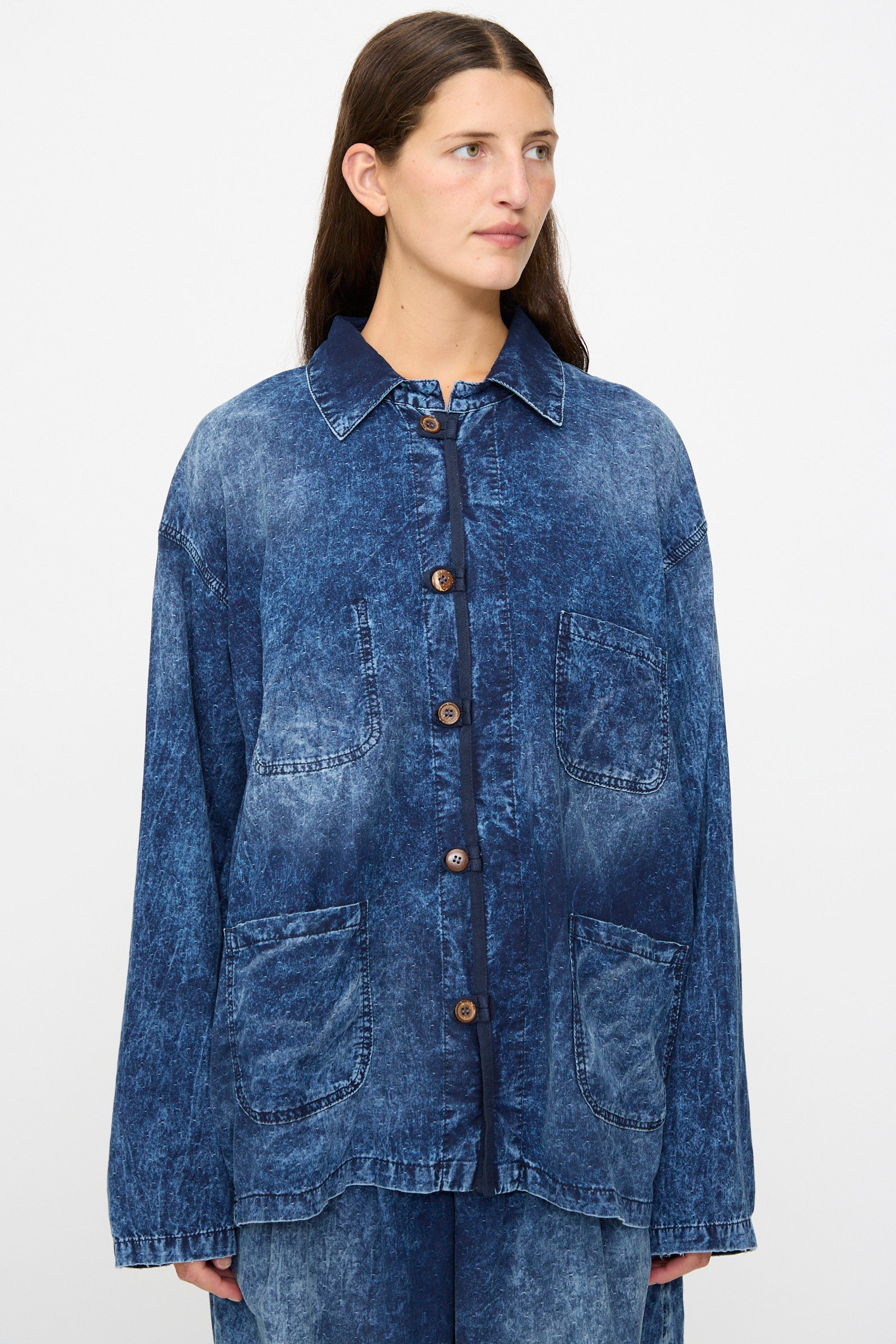 A person wears the Dr. Collectors 6 oz. Cotton New Saigon Shirt Jacket in Indigo—an oversized, acid-wash denim workwear style crafted from indigo cotton with front buttons and four large pockets—while standing against a plain background.