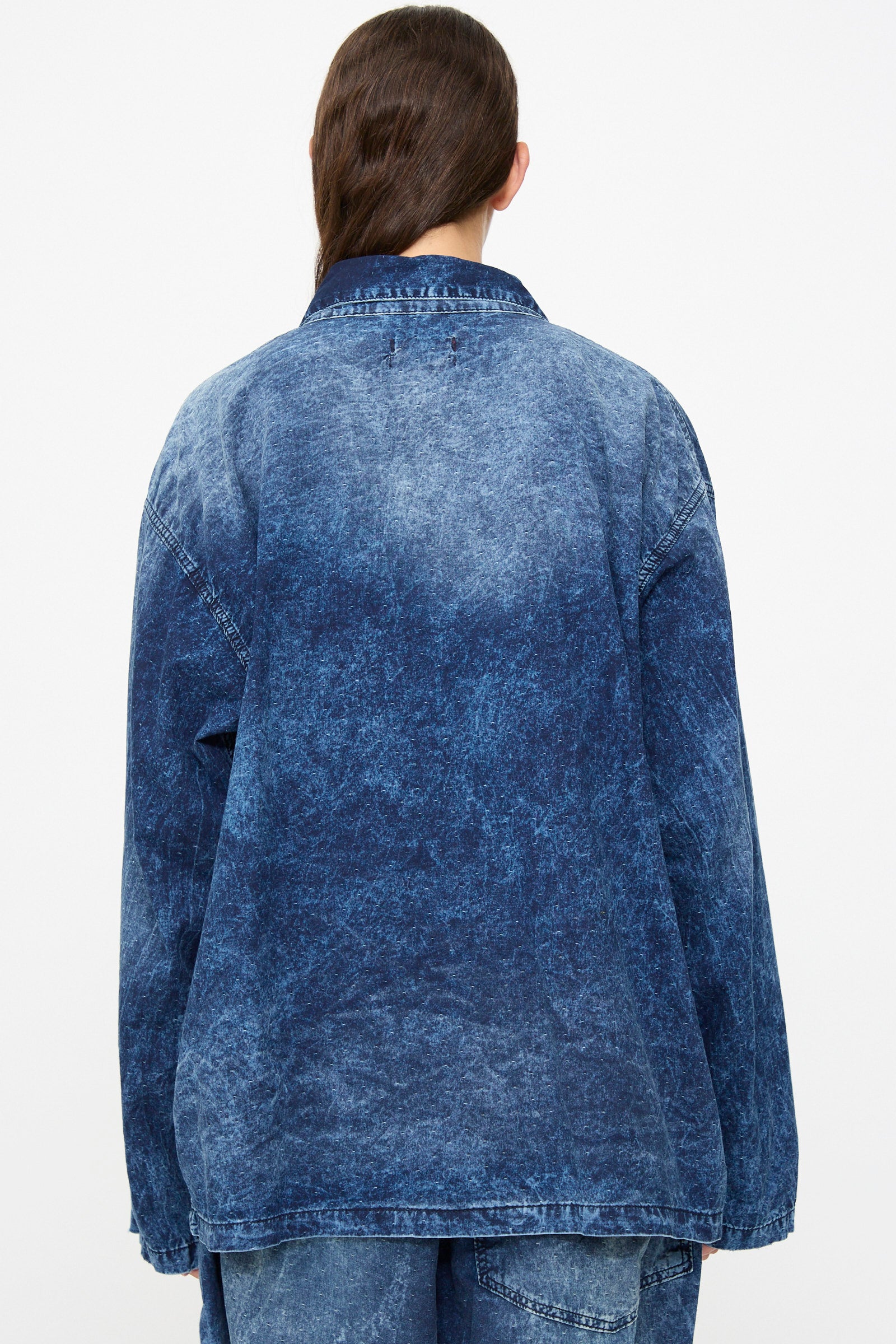 A person with long brown hair is shown from the back against a plain white background, wearing the Dr. Collectors 6 oz. Cotton New Saigon Shirt Jacket in Indigo along with matching denim jeans.
