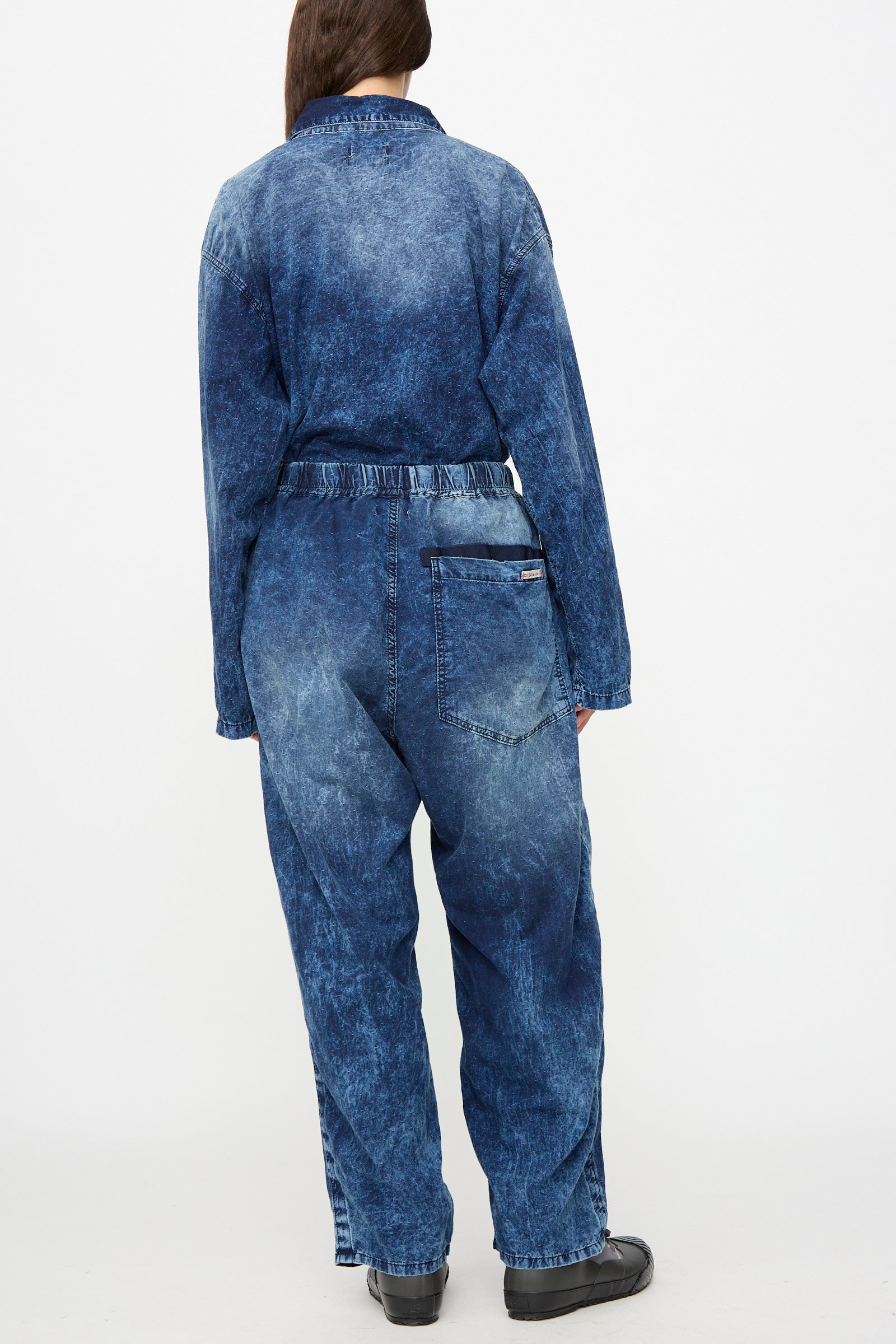 A person is wearing the Dr. Collectors 6 oz. Cotton P43 Kyoto Pant in Sunfaded Indigo, featuring a relaxed fit, paired with black shoes and standing with their back to the camera against a plain white background. 