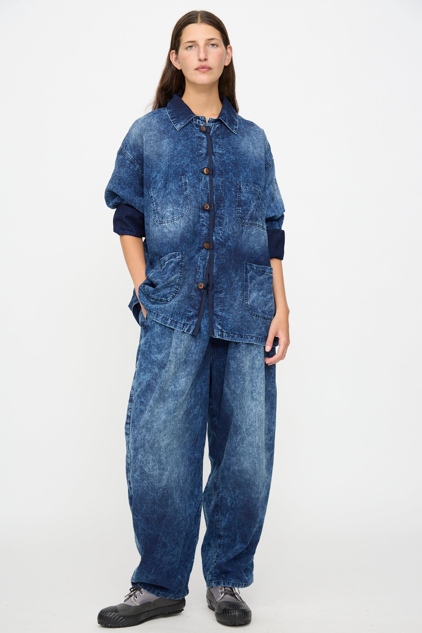 Person standing against a white background wearing Dr. Collectors’ 6 oz. Cotton P43 Kyoto Pant in Sunfaded Indigo, paired with a loose-fitting, button-up indigo cotton denim shirt and black shoes—thoughtfully made in California.