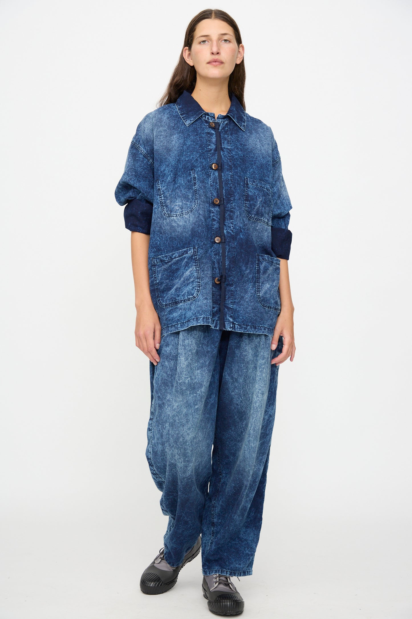 A person wearing wide-leg Dr. Collectors 6 oz. Cotton P43 Kyoto Pant in Sunfaded Indigo, paired with a loose-fitting acid-washed denim jacket, stands against a plain white background.