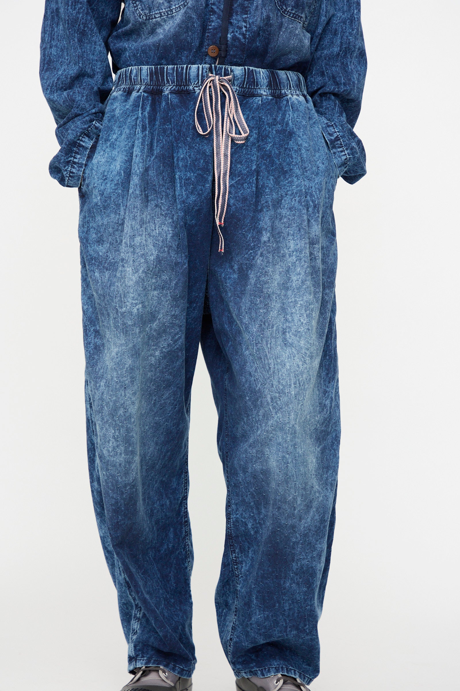 A person is shown from the shoulders down against a plain white background, wearing the Dr. Collectors 6 oz. Cotton P43 Kyoto Pant in Sunfaded Indigo—an acid-wash finish, loose-fitting pant with a drawstring waist and hands in pockets.