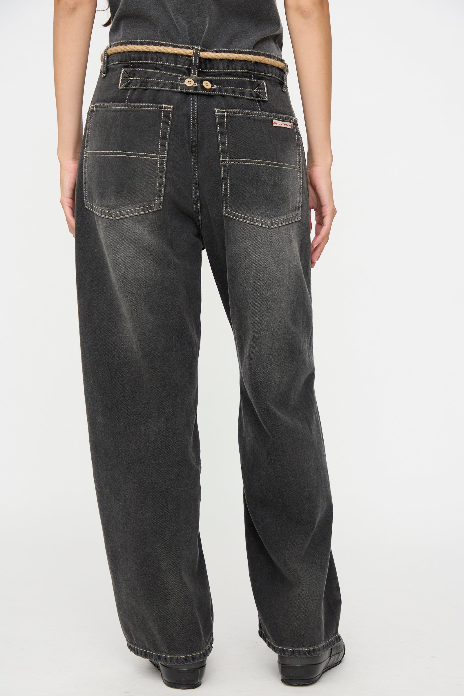 A person is shown from the back against a plain white background, wearing Dr. Collectors’ 9 oz. Denim P84 Dungaree Pant in Sunfaded Black, featuring a loose fit, large back pockets, and a braided hemp rope belt.