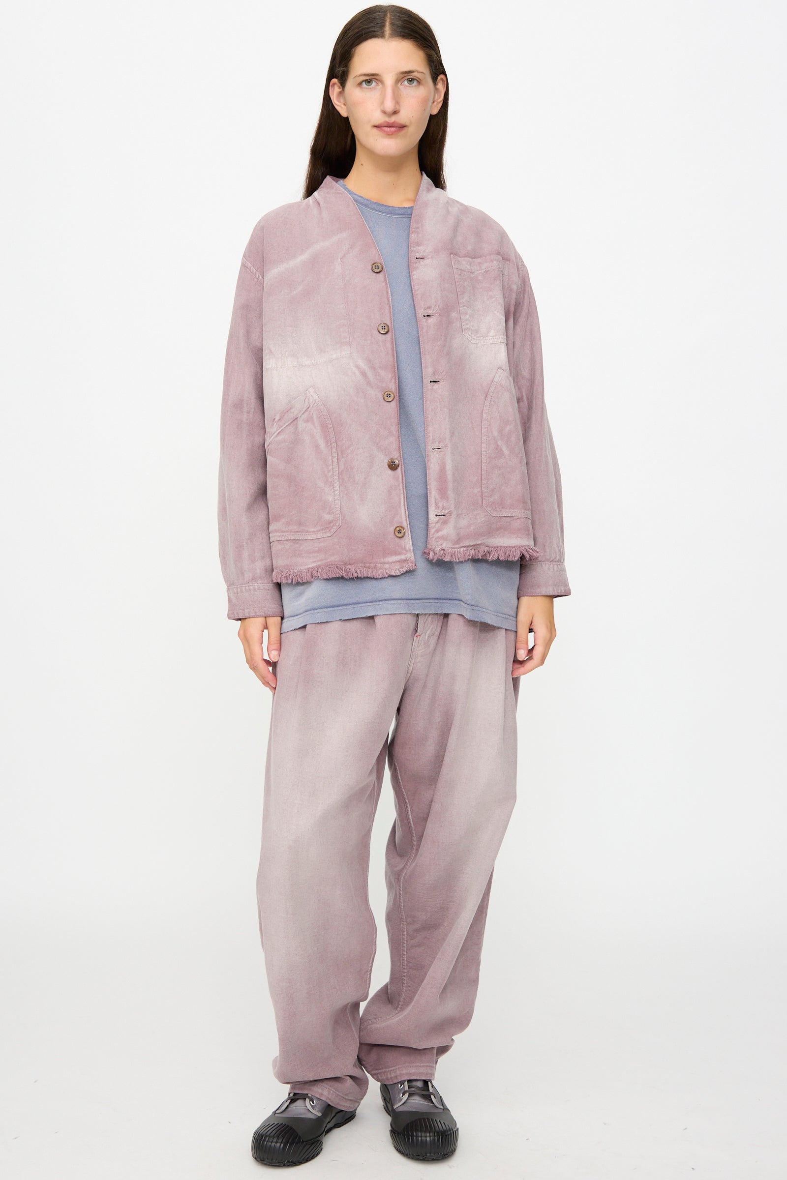 A person stands against a plain background wearing the Dr. Collectors 9 oz. Okinawa Jacket in Sunfaded Dusty Orchid, an oversized vintage-inspired piece crafted from a soft linen cotton blend and paired with matching loose pants over a blue shirt, finished with black shoes.