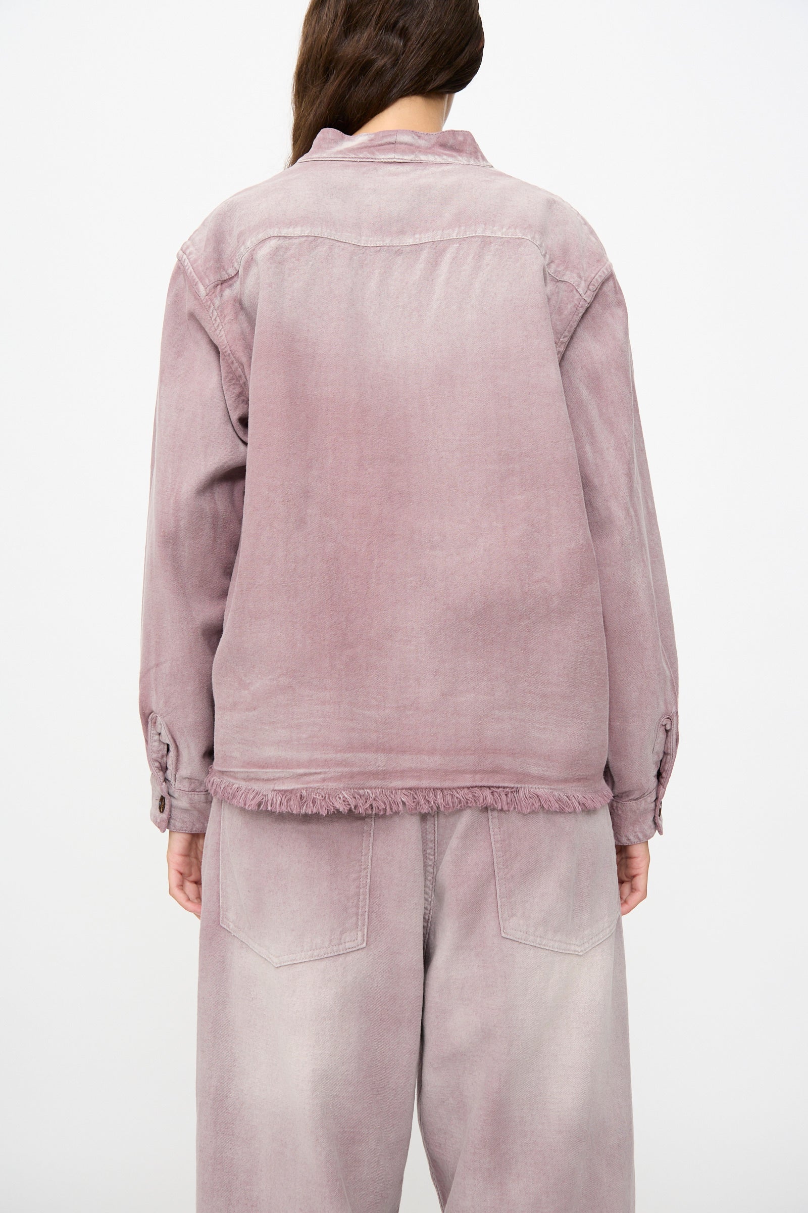 A person facing away, wearing the Dr. Collectors 9 oz. Okinawa Jacket in Sunfaded Dusty Orchid—a loose-fitting, light purple linen-cotton blend denim jacket—paired with matching pants featuring a frayed hem and visible back pockets, set against a plain white background.