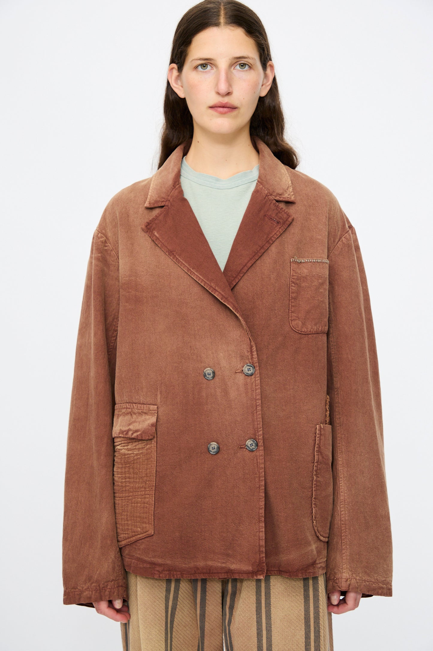 A person with long brown hair wears the Dr. Collectors Bogart Jacket in Nuts over a green shirt and striped beige pants, standing against a plain background.