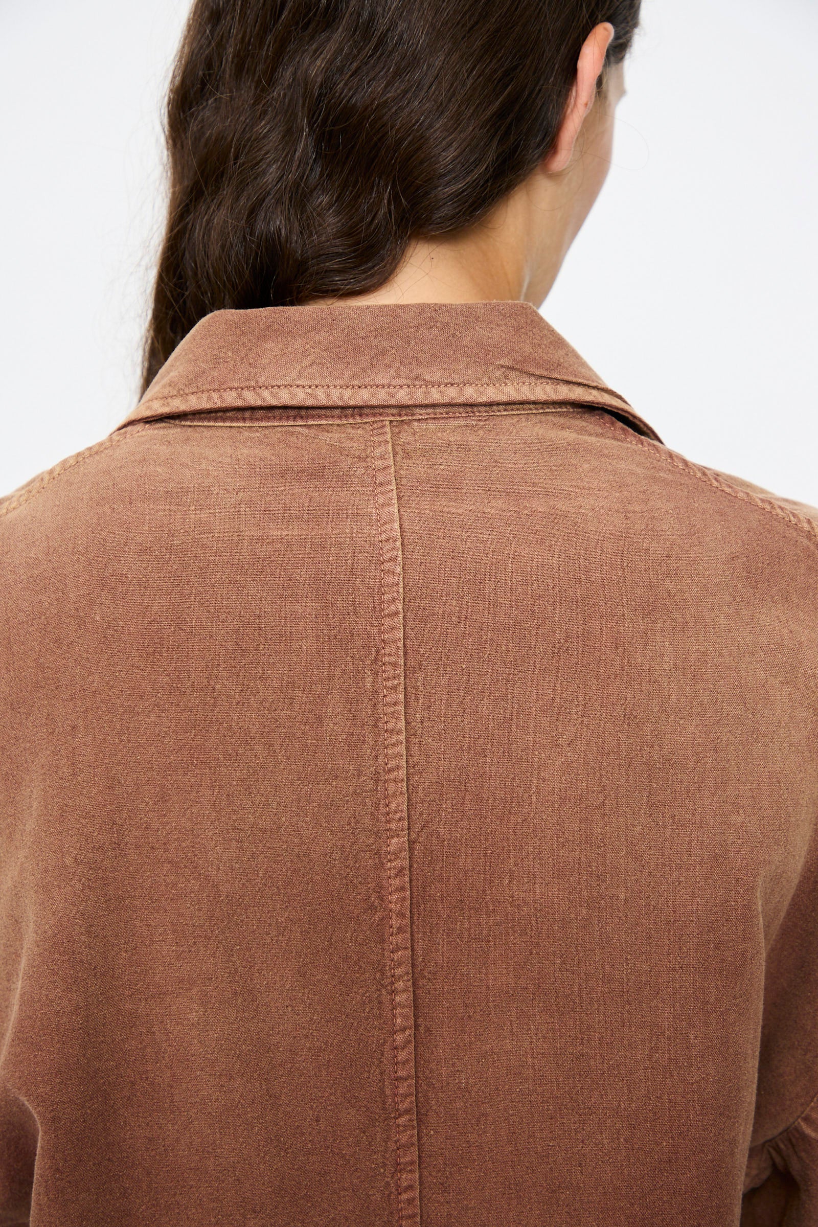 A person with long brown hair is seen from behind, wearing the Dr. Collectors Bogart Jacket in Nuts—a vintage-style brown collared jacket with visible seams down the center and shoulders.