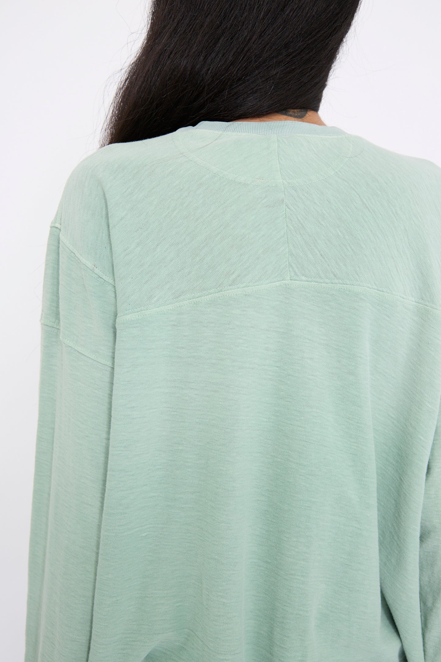 A person with long dark hair, seen from the back, wearing a Cotton Derrick Tee in Sunfaded Smoke Green by Dr. Collectors, crafted from recycled cotton.