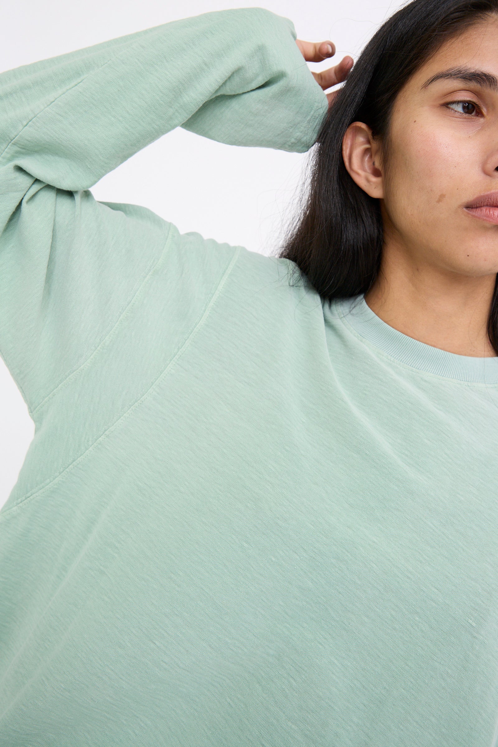 A person wearing the Sunfaded Smoke Green Cotton Derrick Tee from Dr. Collectors, made from recycled cotton in a relaxed fit style, stands against a plain background with an arm raised. 