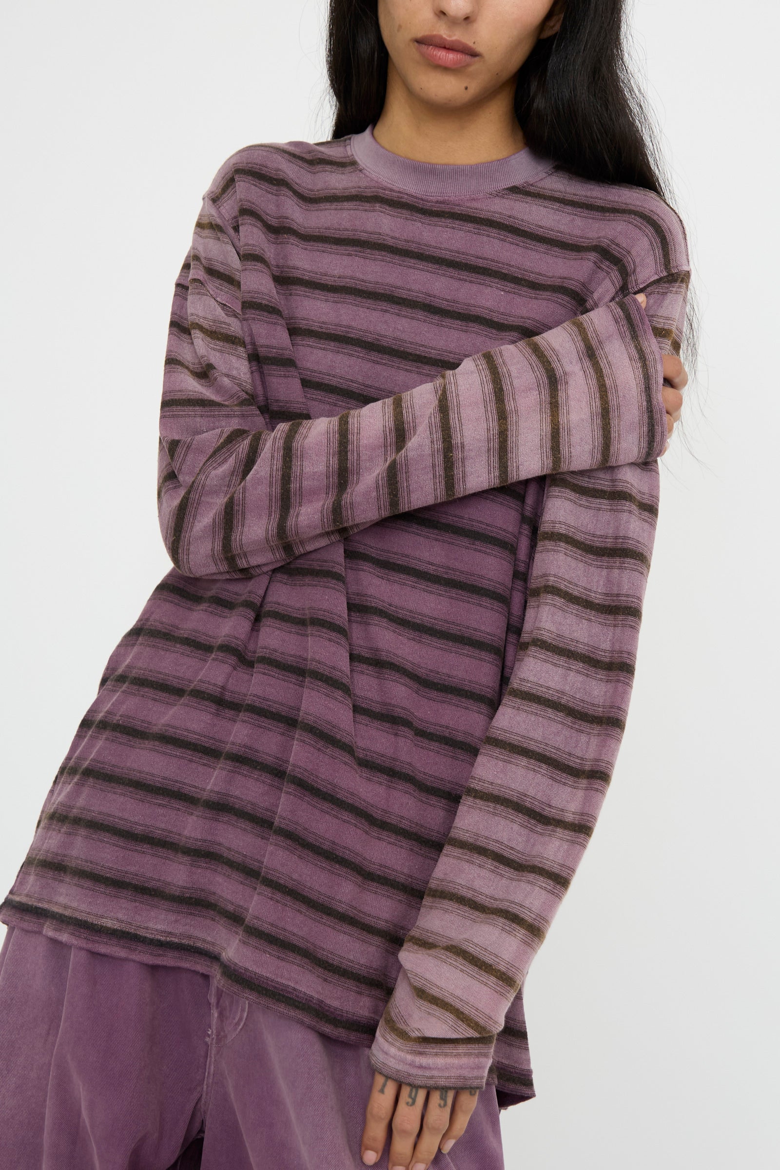 A person crosses their arms while wearing Dr. Collectors' Hemp and Cotton Derrick Tee in Stripes of Sunfaded Mauve, paired with matching pants against a white background. 