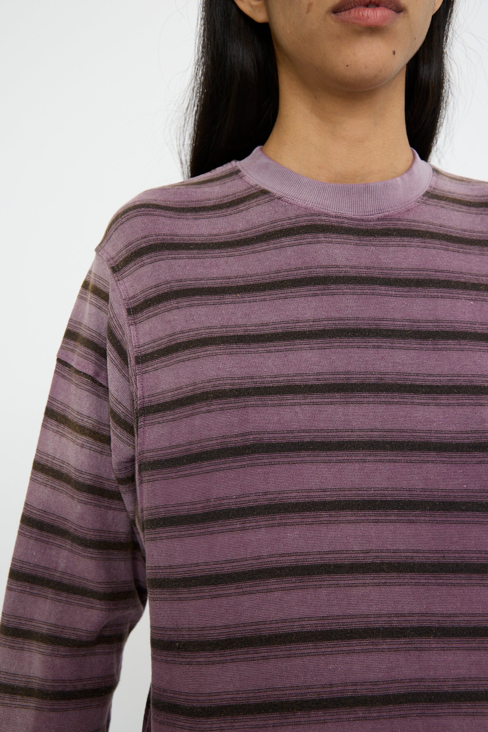 A close-up of a person wearing a Dr. Collectors Hemp and Cotton Derrick Tee Stripes in Sunfaded Mauve, featuring a cozy crew neck and crafted from recycled cotton against a white background. 