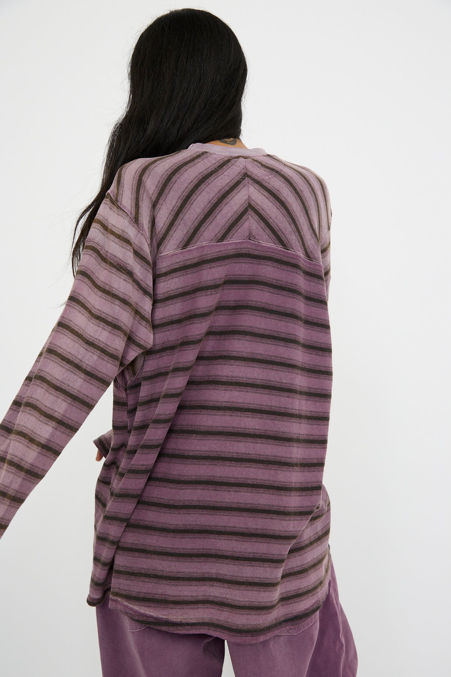 A person wearing the Hemp and Cotton Derrick Tee Stripes in Sunfaded Mauve by Dr. Collectors, featuring purple and black stripes, with their back facing the camera.