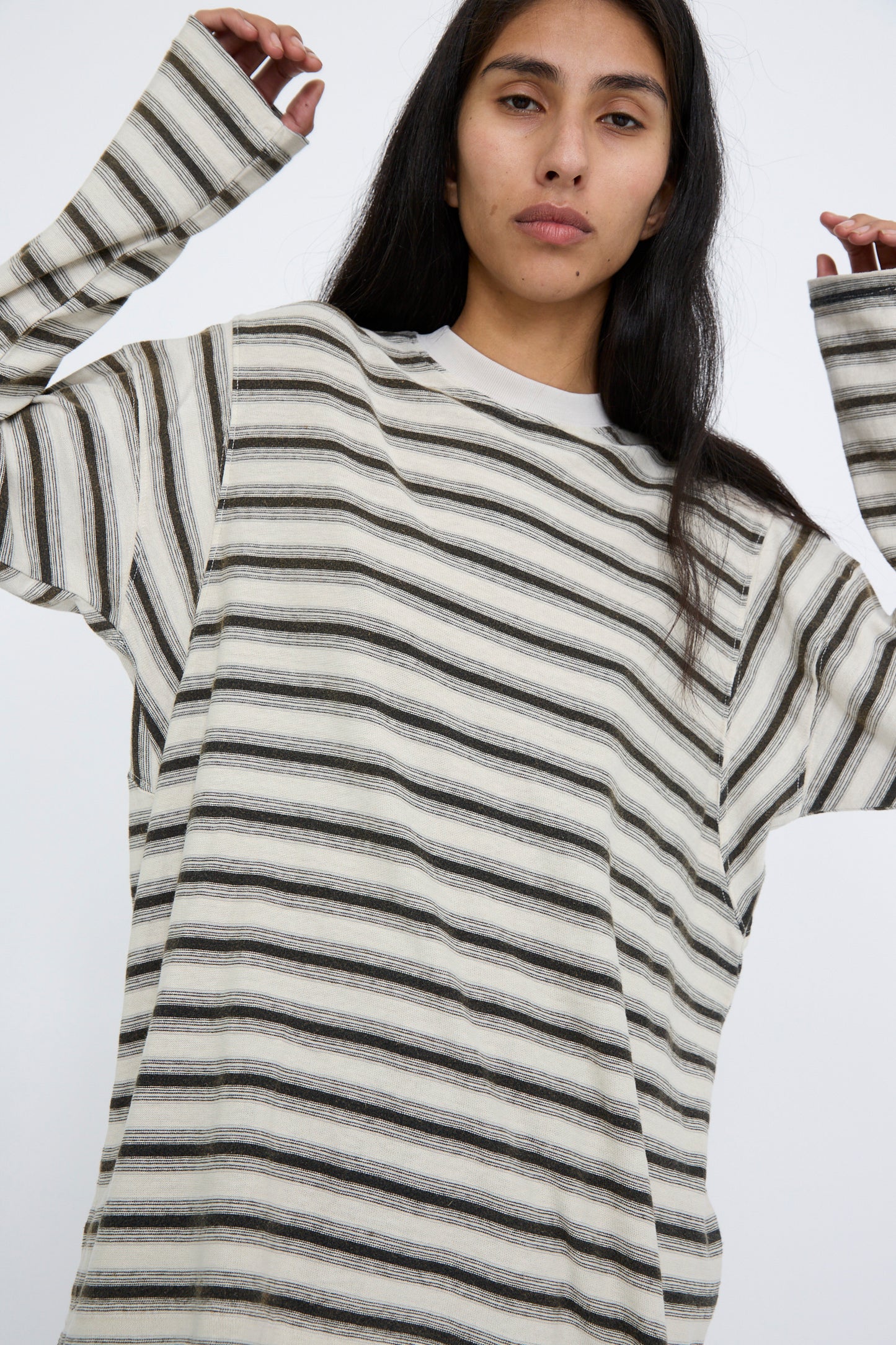 A person wearing the Hemp and Cotton Derrick Tee Stripes in Sunfaded Stone by Dr. Collectors, with a relaxed fit and long sleeves, made from recycled cotton, has their hands raised slightly against a white background. 