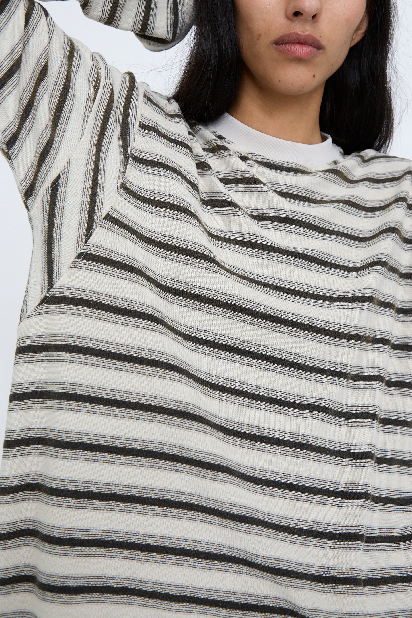 A person wearing the Dr. Collectors Hemp and Cotton Derrick Tee Stripes in Sunfaded Stone, styled in a relaxed fit, stands with their arm raised, partially covering their face against a plain background. 