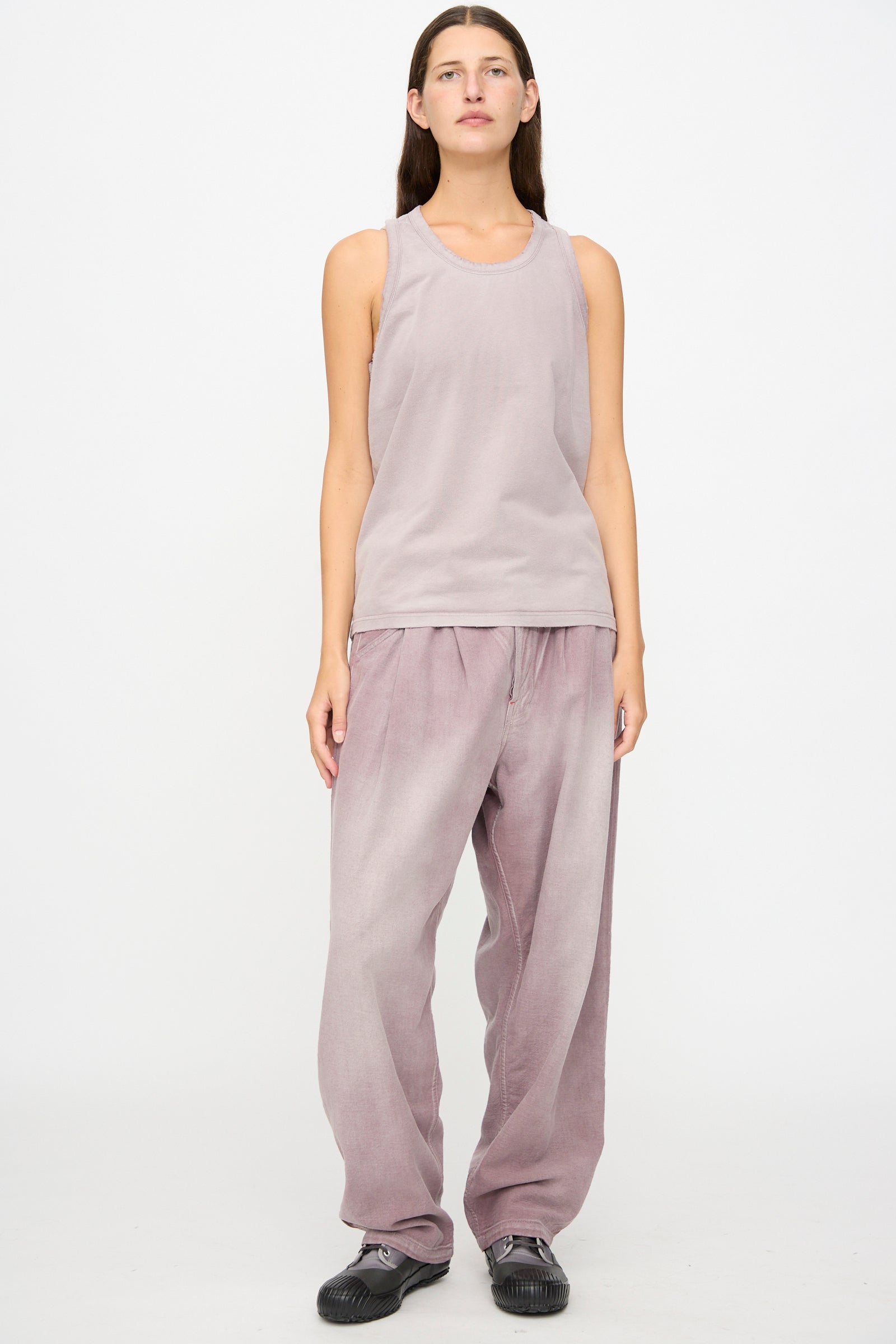 Person standing against a white background wearing the Marcel Tank in Sunfaded Dusty Orchid by Dr. Collectors, loose mauve pants dyed with plant-based dyes, and black shoes.