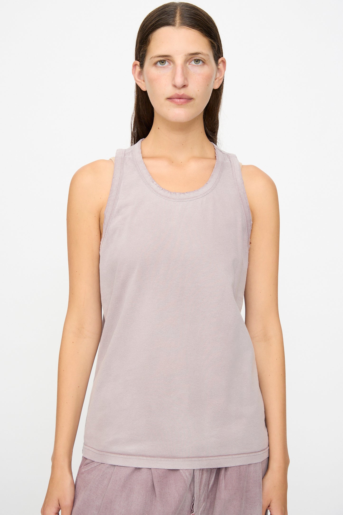 A person with straight brown hair wears the Dr. Collectors Marcel Tank in Sunfaded Dusty Orchid, a light mauve sleeveless organic cotton top, along with matching mauve pants, standing against a plain white background and facing forward with a neutral expression.
