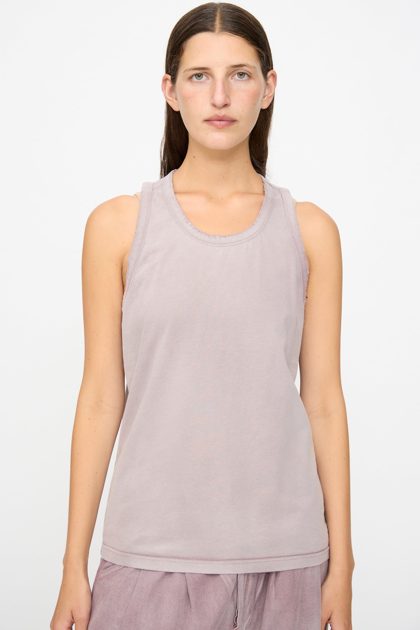 A person with straight brown hair wears the Dr. Collectors Marcel Tank in Sunfaded Dusty Orchid, a light mauve sleeveless organic cotton top, along with matching mauve pants, standing against a plain white background and facing forward with a neutral expression.