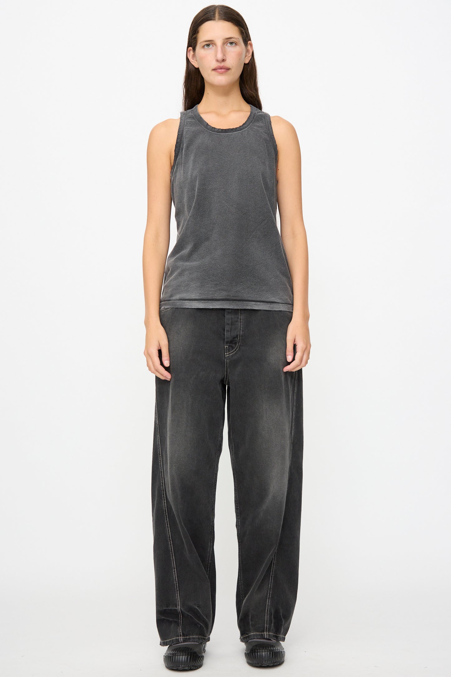A person stands facing forward, wearing the Marcel Tank in Sunfaded Smoke Black by Dr. Collectors and loose-fitting black jeans with black shoes, against a plain white background.