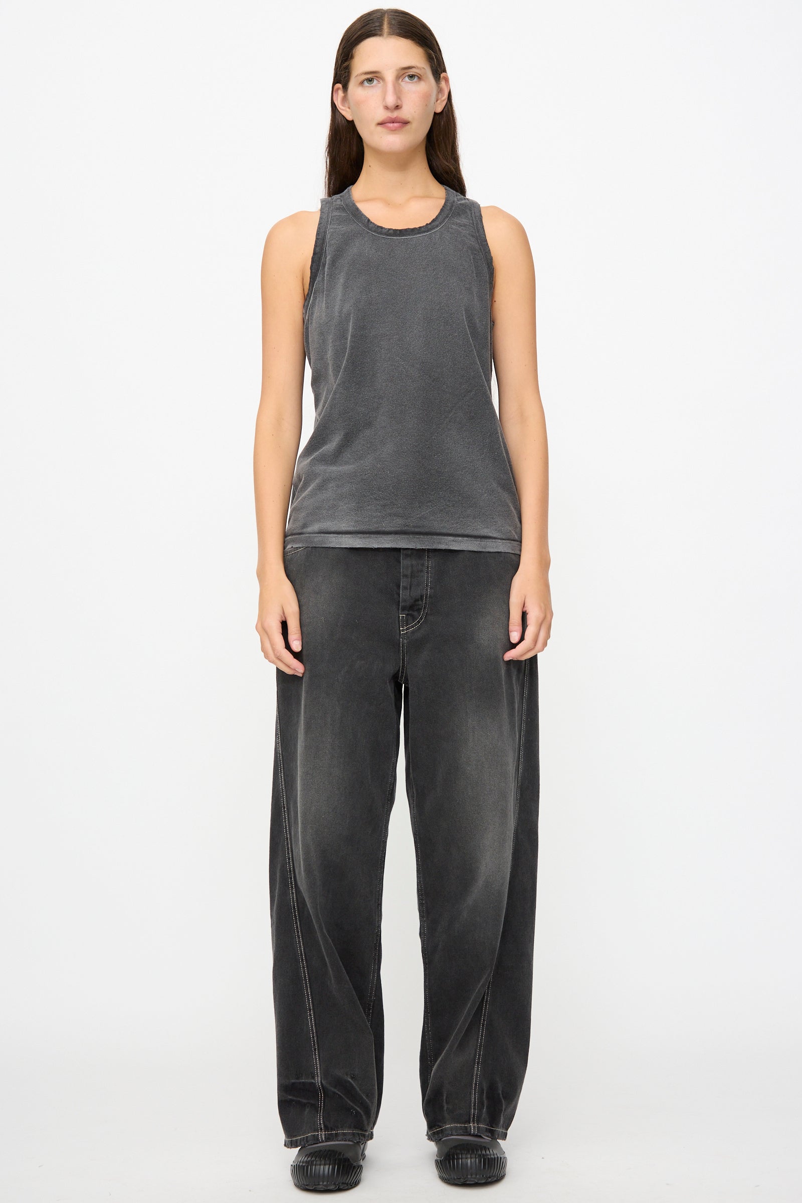 A person stands facing forward, wearing the Marcel Tank in Sunfaded Smoke Black by Dr. Collectors and loose-fitting black jeans with black shoes, against a plain white background.