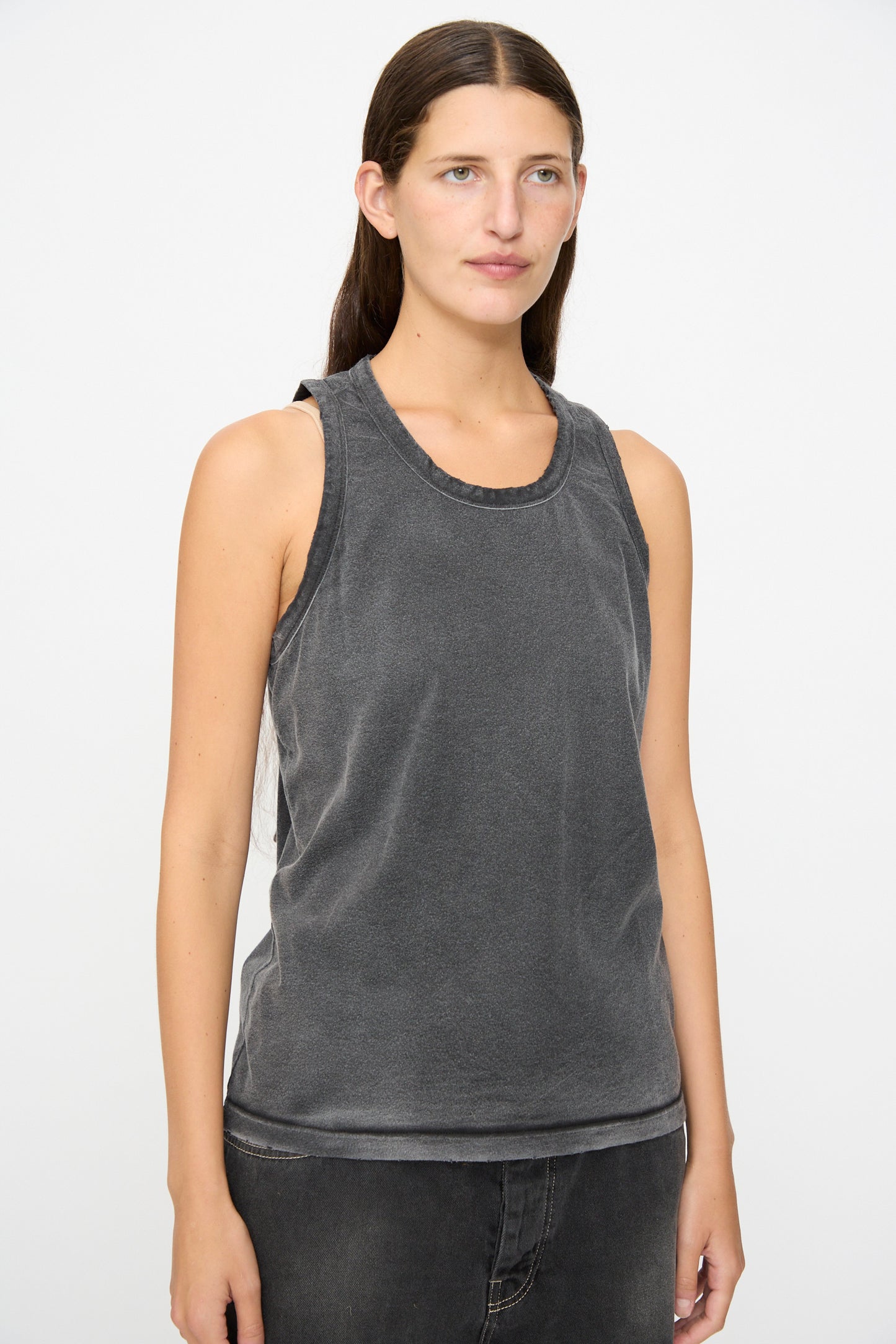 A person with long dark hair wears the Dr. Collectors Marcel Tank in Sunfaded Smoke Black—an organic cotton, sleeveless tank top styled with dark pants—standing against a plain light background.