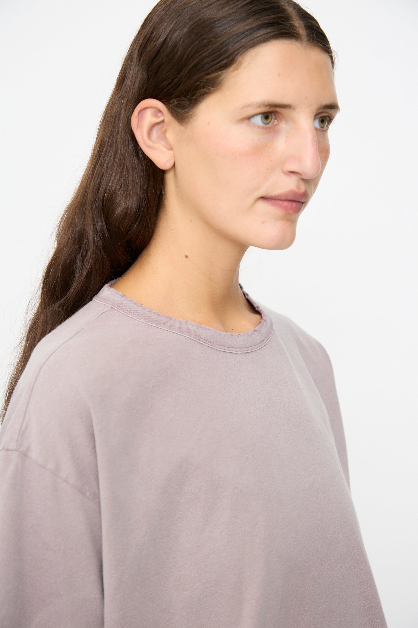 A person with long brown hair and a neutral expression is shown in profile against a plain white background, wearing Dr. Collectors’ Model T sweatshirt in Sunfaded Dusty Orchid, crafted from recycled cotton for a loose fit.