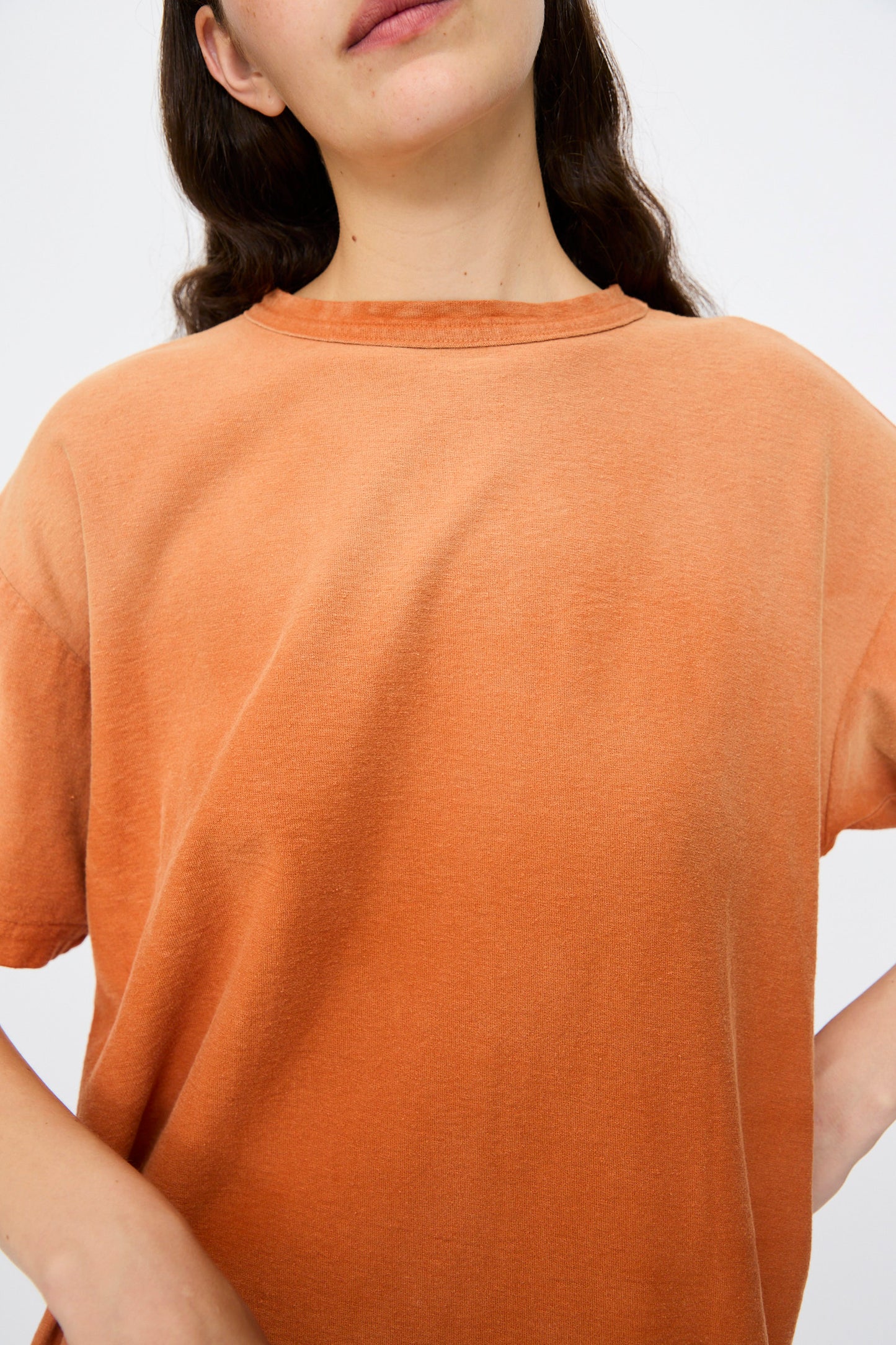 A person wears the Dr. Collectors Model T. Sunfaded in Rust—an orange, vintage-look loose fit tee—shown from shoulders to mouth against a plain backdrop.