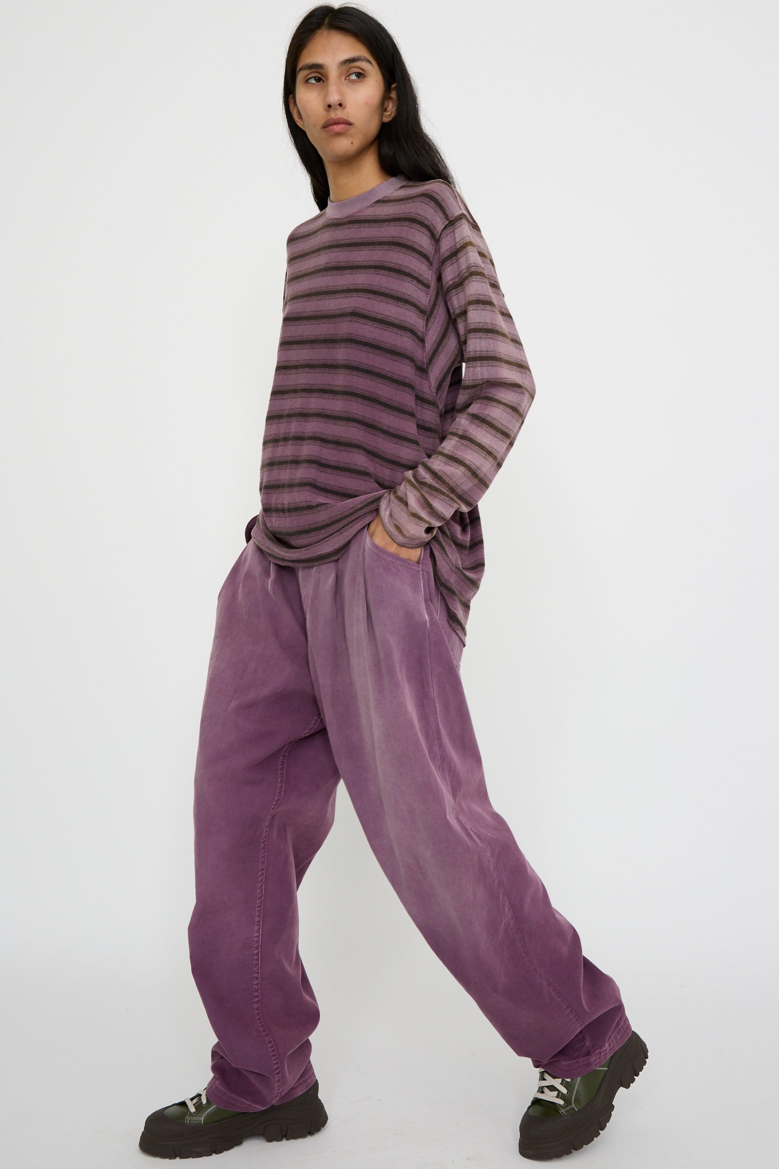 A person wearing a striped long-sleeve shirt and the Dr. Collectors P40 Z Boy's Twill Pant in Sunfaded Mauve, which features a loose straight-leg, oversized silhouette made from Japanese cotton, stands against a plain background with hands in their pockets.