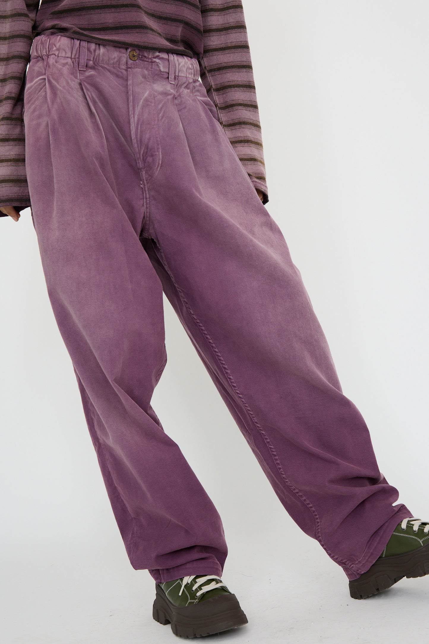 A person stands against a light background wearing the P40 Z Boy's Twill Pant in Sunfaded Mauve from Dr. Collectors, made of Japanese cotton, along with a striped long-sleeve shirt, paired with chunky dark green shoes against a white background.