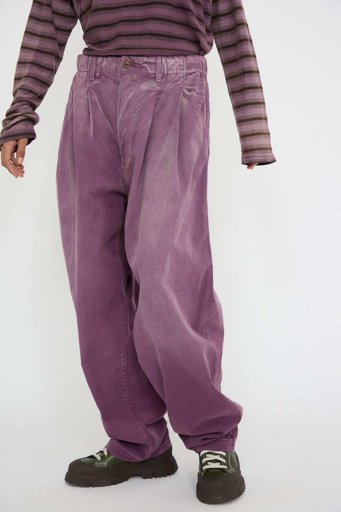 A person wearing a striped long-sleeve shirt and black shoes stands against a plain background, showcasing the Dr. Collectors P40 Z Boy's Twill Pant in Sunfaded Mauve, featuring an oversized Japanese cotton design with a loose straight leg.