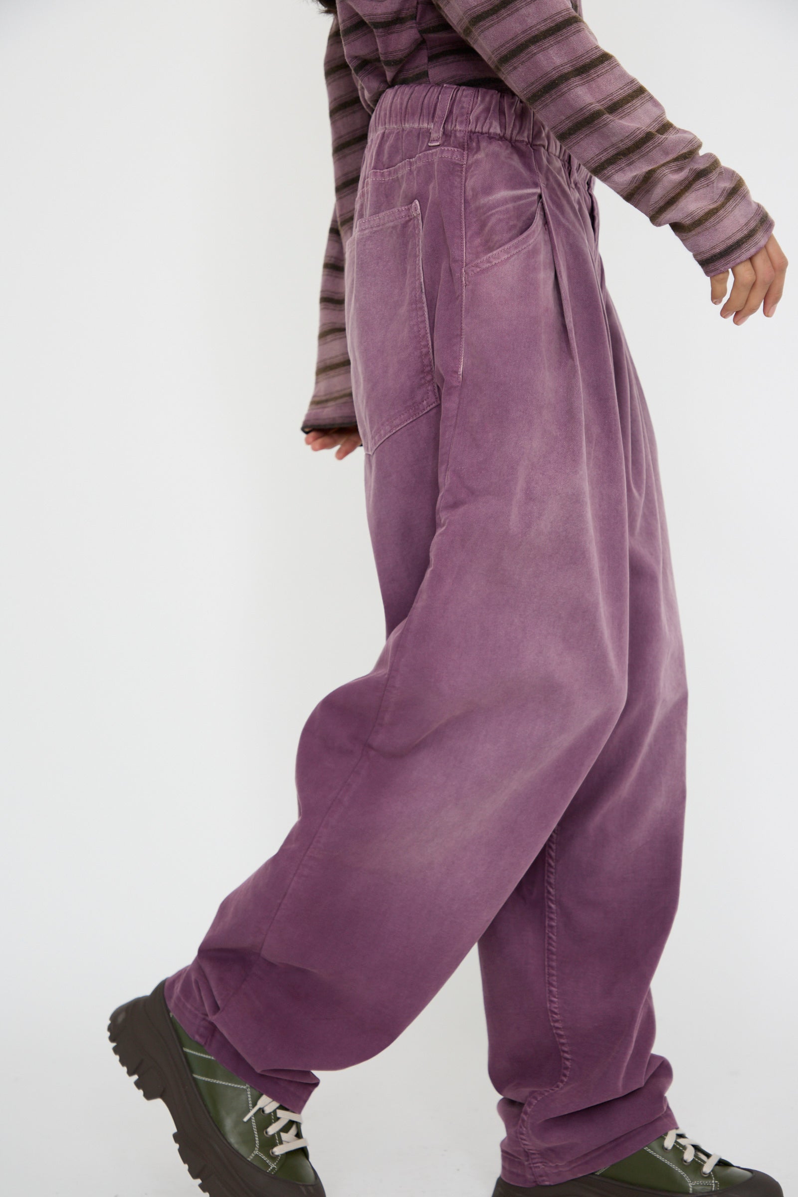 A person walks in P40 Z Boy's Twill Pants in Sunfaded Mauve by Dr. Collectors, paired with a striped top and showcasing chunky dark green boots against a white background. 