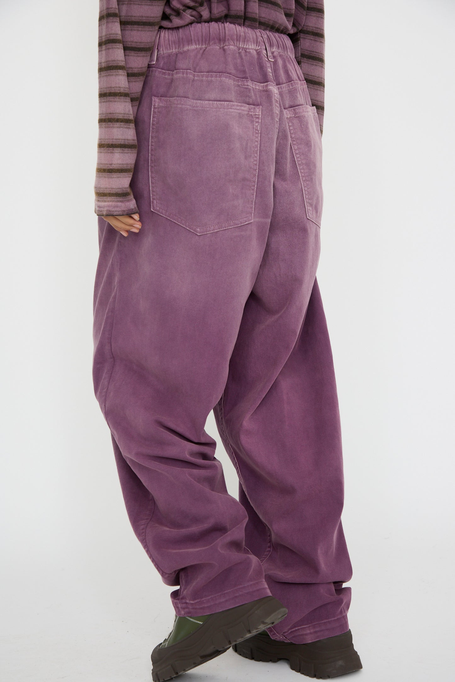 A person is seen from the back against a plain background, draped in oversized P40 Z Boy's Twill Pants in Sunfaded Mauve by Dr. Collectors and a striped top.