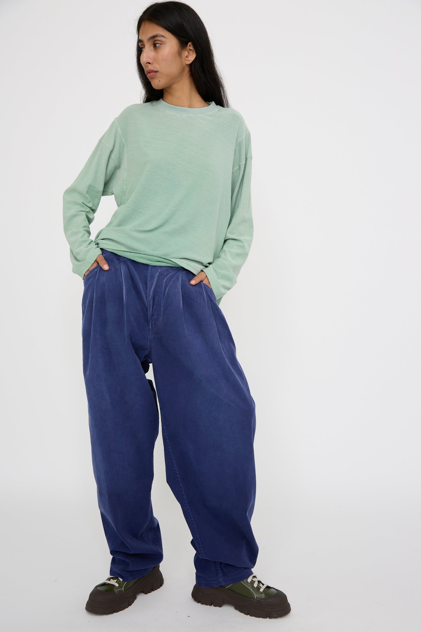 Standing against a plain white background, a person is dressed in a light green sweater paired with Dr. Collectors' P40 Z Boy's Twill Pant in Sunfaded Sailor Blue. 